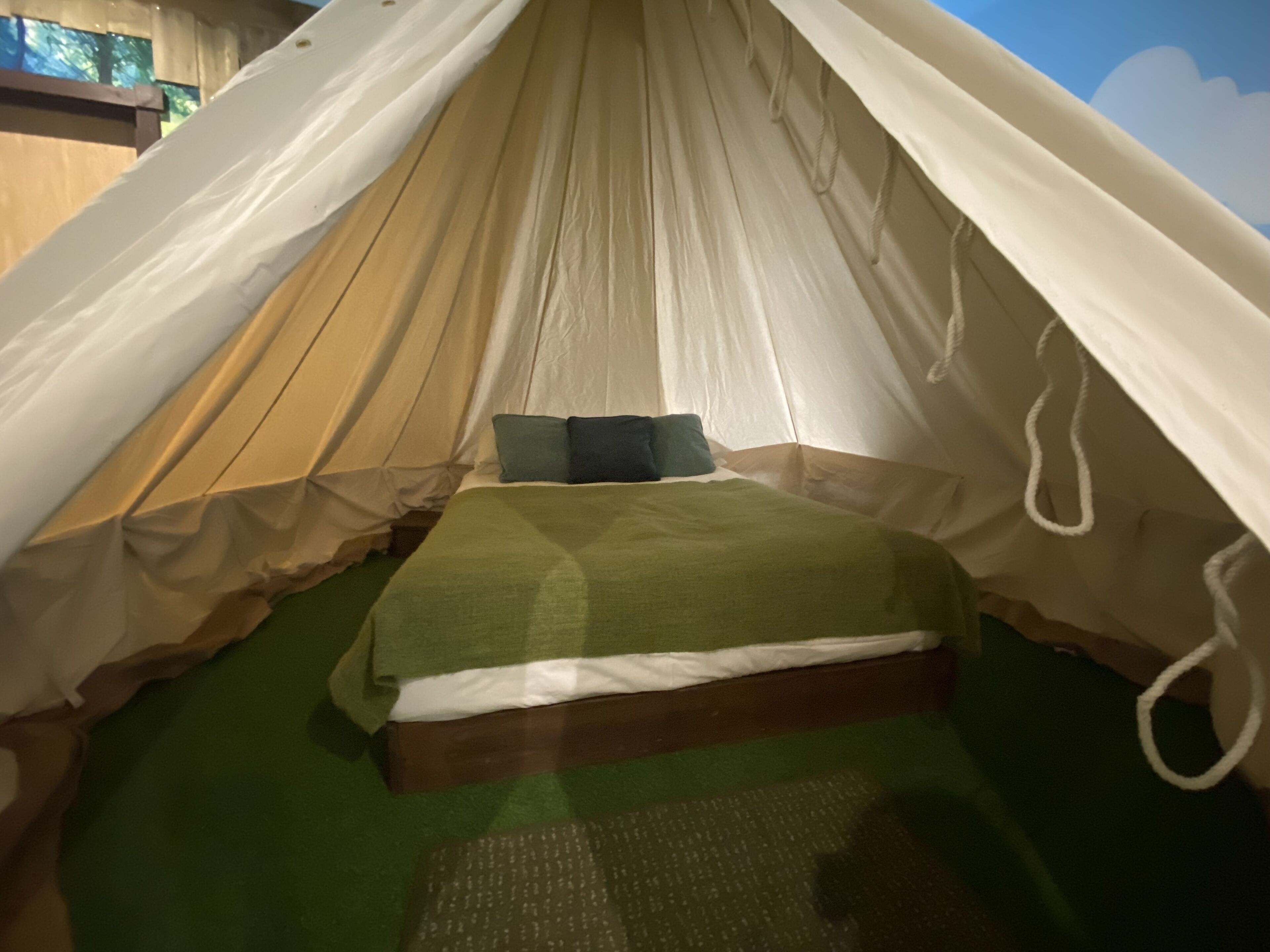 Una tienda de campaña con una cama, ropa de cama verde y vistas al exterior.