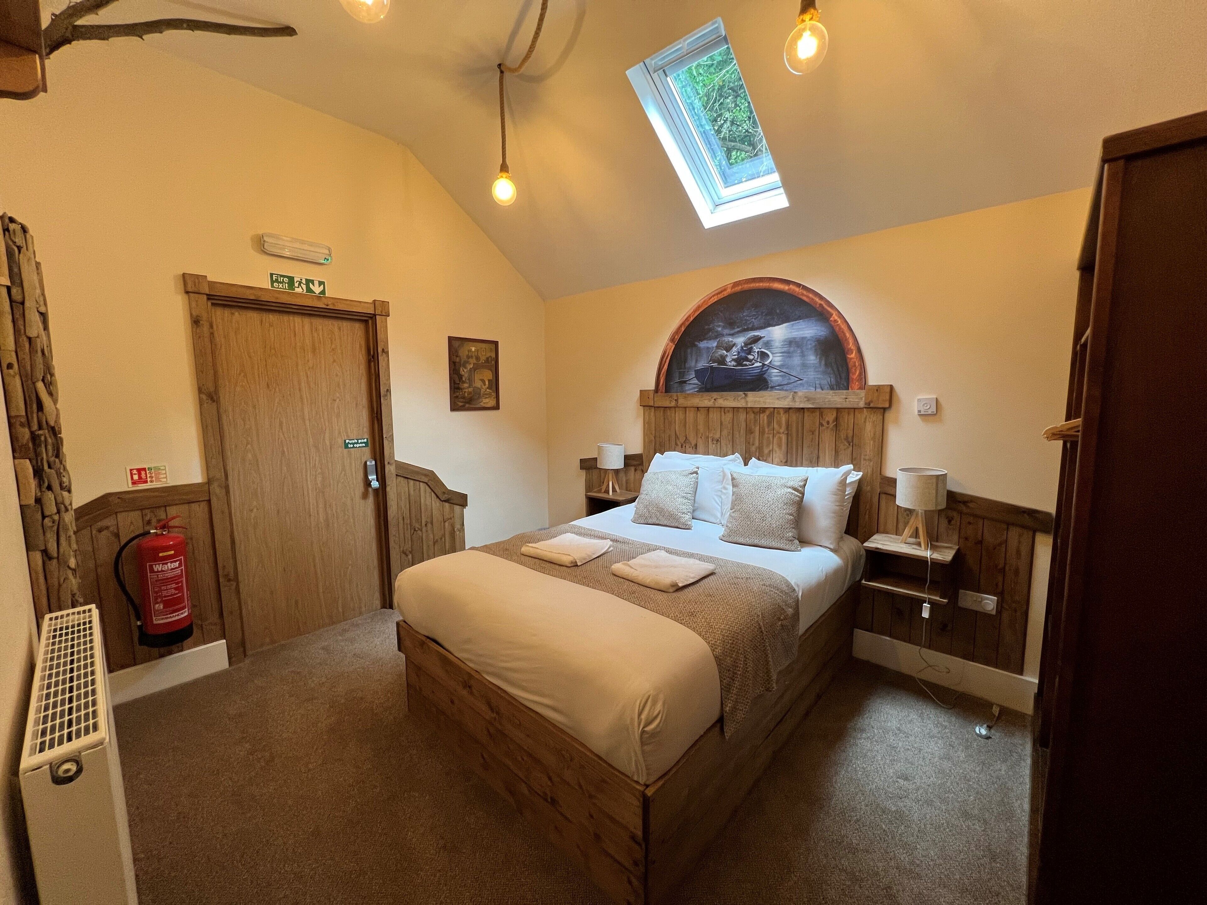 A bedroom with a wooden bed, a skylight, a fire exit sign, a water fire extinguisher, and a rustic decor.