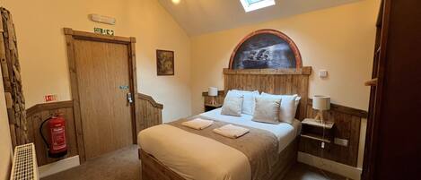 A bedroom with a wooden bed, a skylight, a fire exit sign, a water fire extinguisher, and a rustic decor.