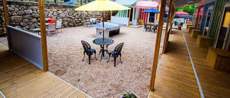 An outdoor patio area with a wooden deck, a table with chairs, and a yellow umbrella.