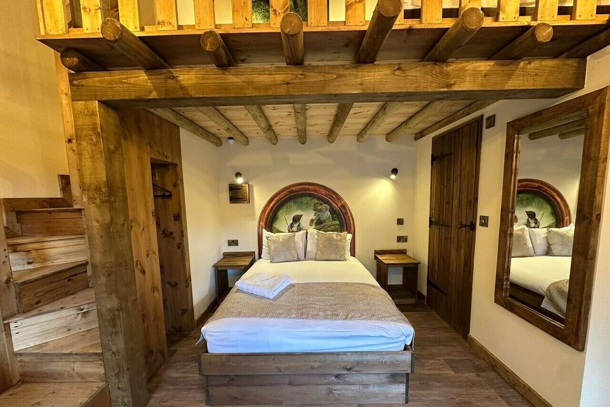 A bedroom with a wooden staircase, a bed with a headboard, and a mirror on the wall.