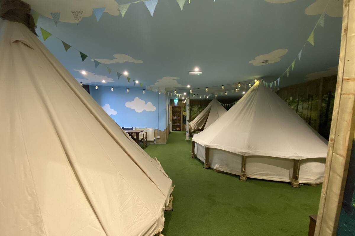 A room with multiple white tents, green carpet, and a blue wall with cloud patterns.