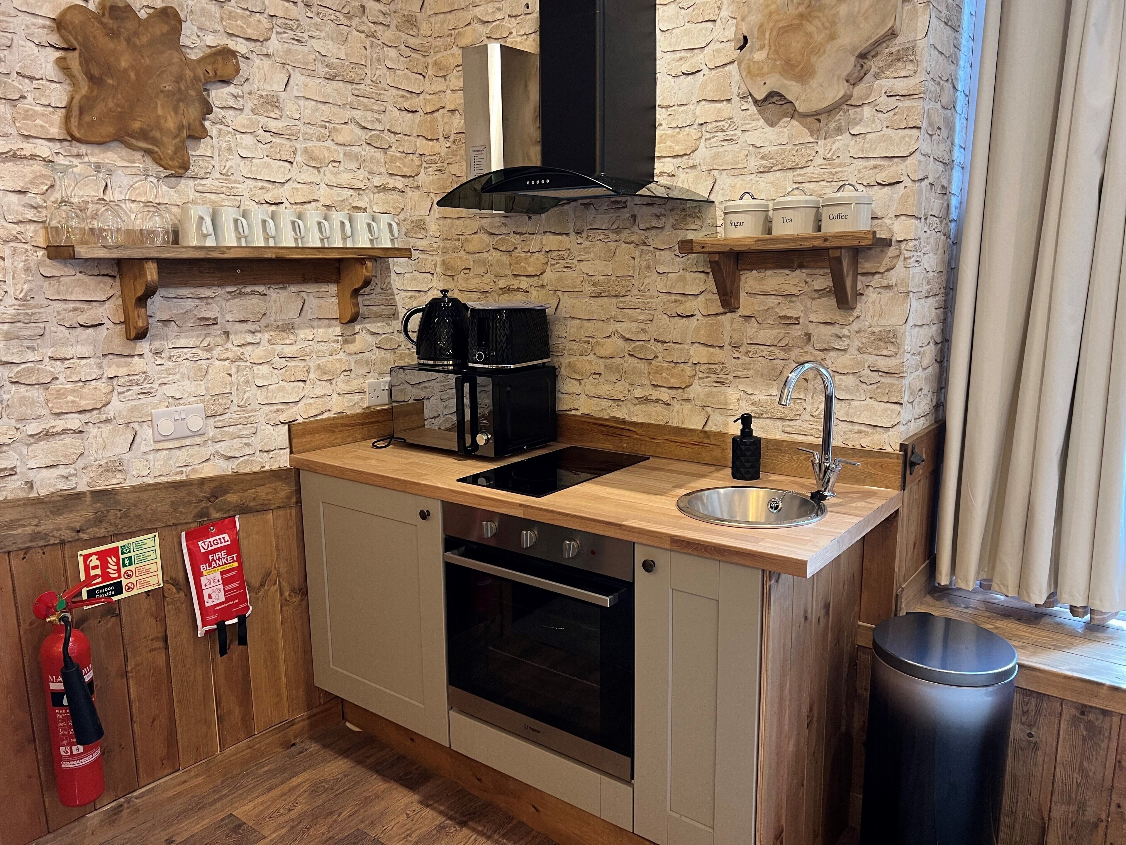 Una cocina compacta con pared de piedra, encimera de madera, pileta, estufa y cafetera.