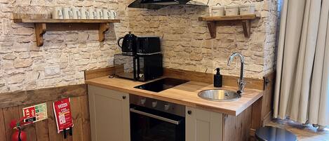 Una cocina compacta con pared de piedra, encimera de madera, pileta, estufa y cafetera.