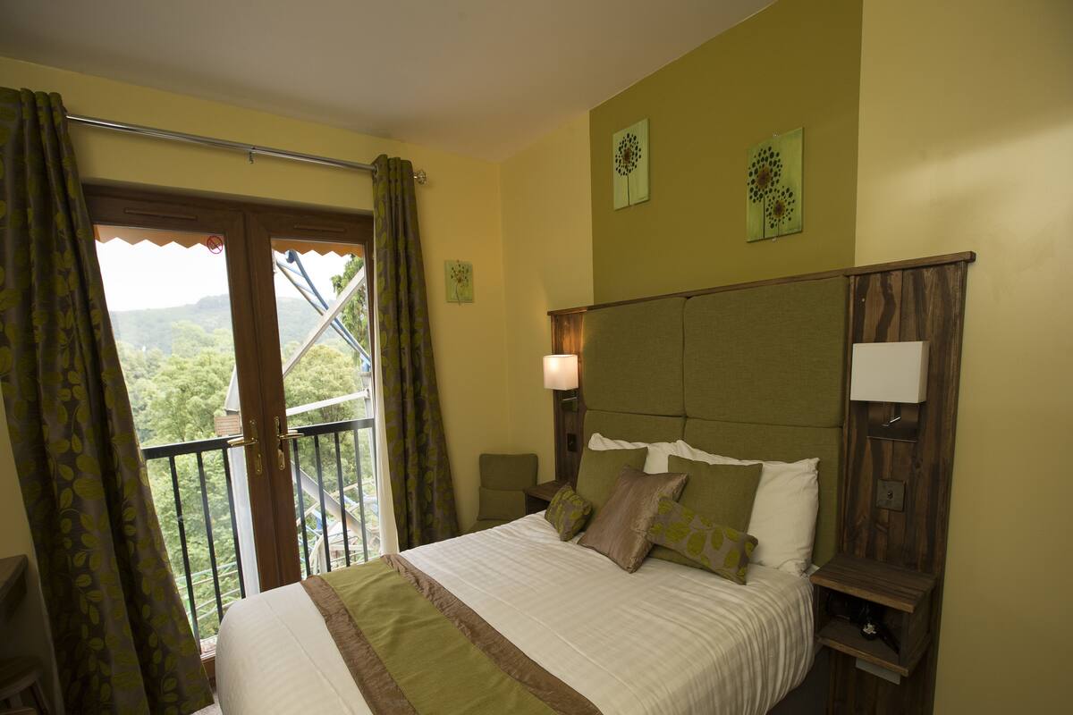 A hotel room with a bed, a nightstand, a lamp, a chair, and a balcony with curtains.