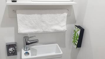 Un baño con un lavamanos blanco, un espejo encima, una toalla colgada en un perchero y un inodoro.