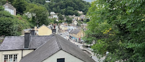 A town with buildings on a hillside, a street with cars, and trees.