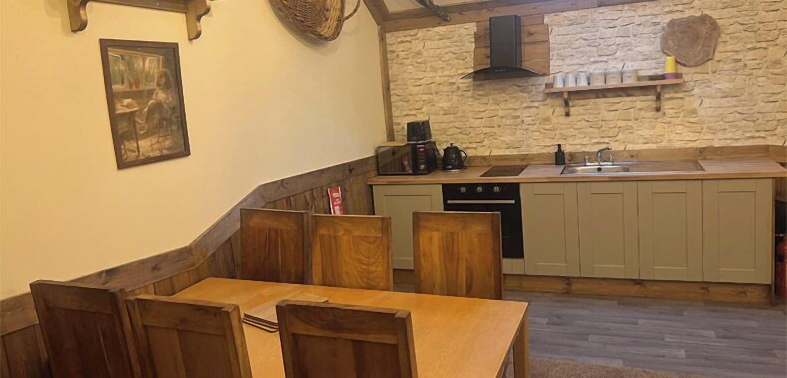 A cozy kitchen with wooden cabinets, a stone wall, and a dining area with a wooden table and chairs.