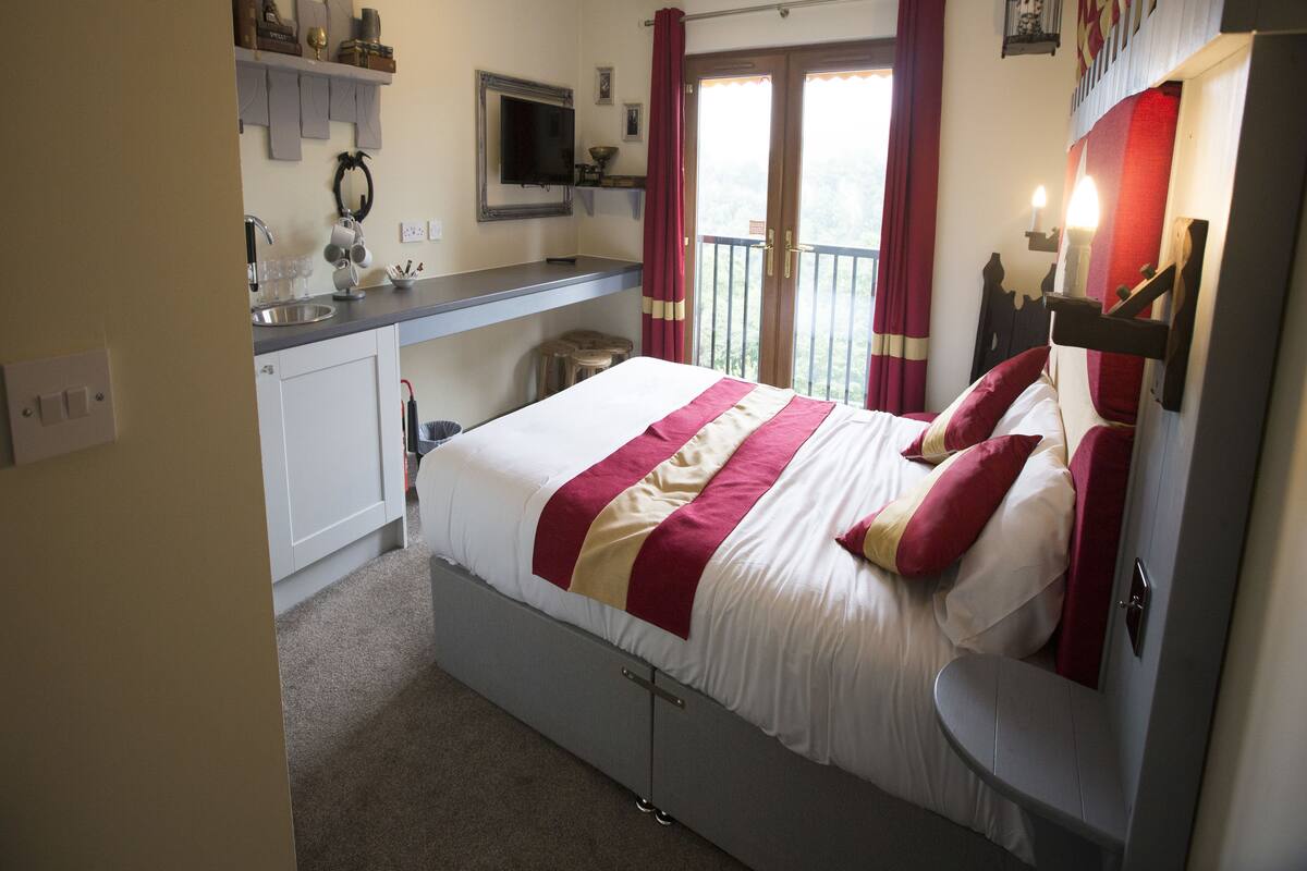 A bedroom with a bed, a desk, a television, and a balcony with curtains.