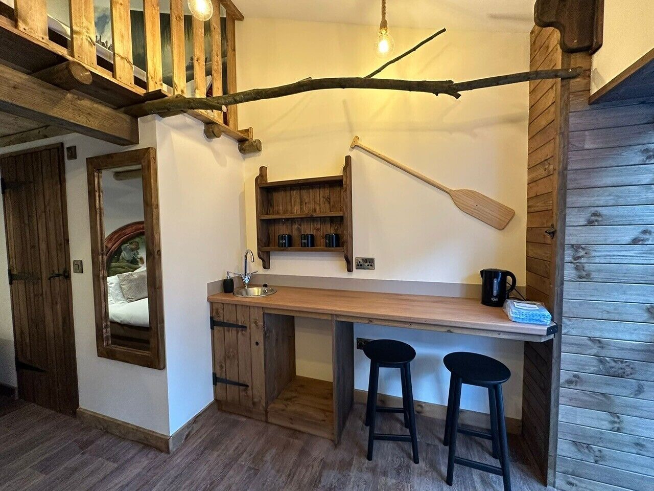 A rustic kitchen with wooden shelves, a hanging pot, and a wooden dining table with two stools.