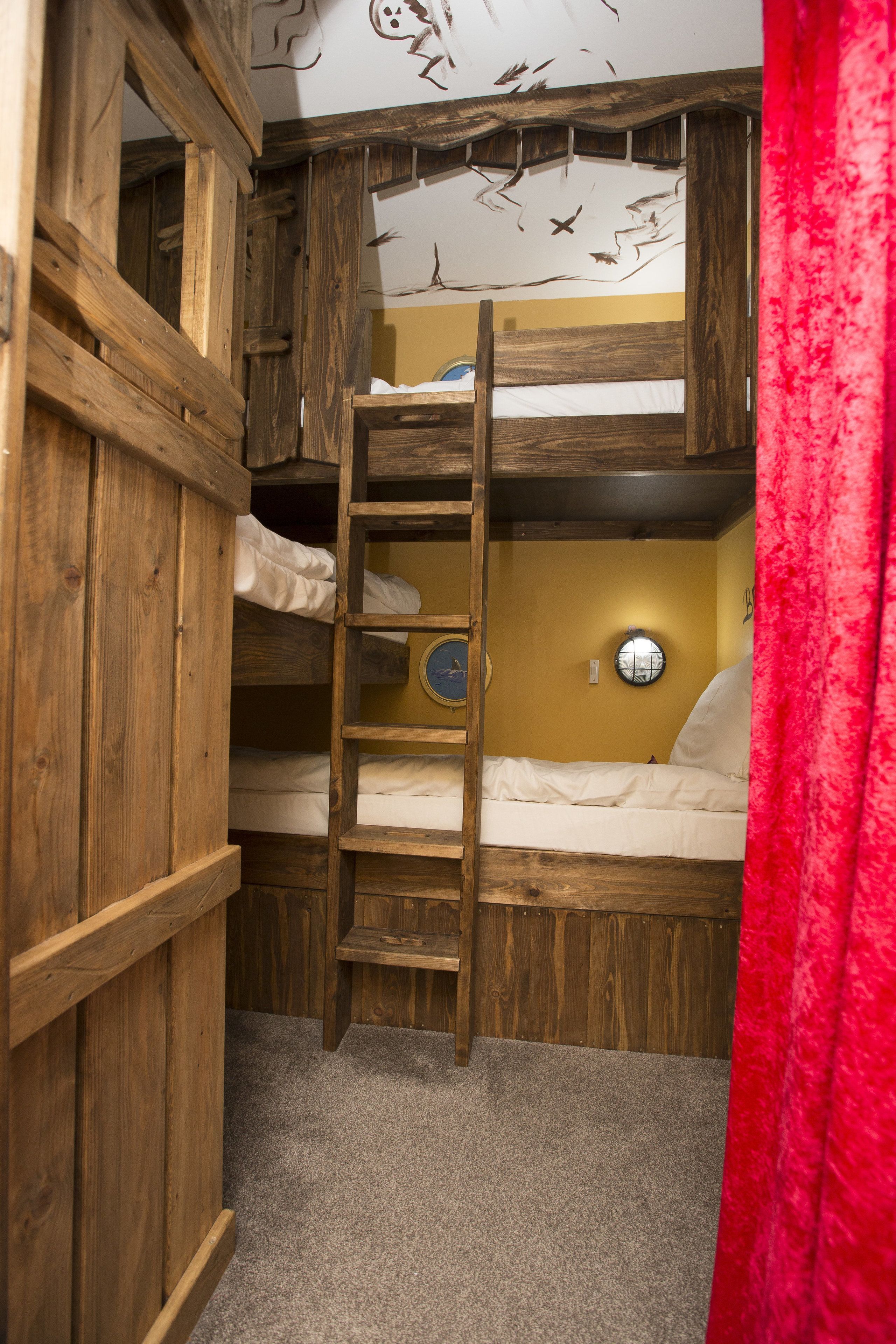 A bunk bed room with a wooden ladder, a round wall clock, and a red curtain.