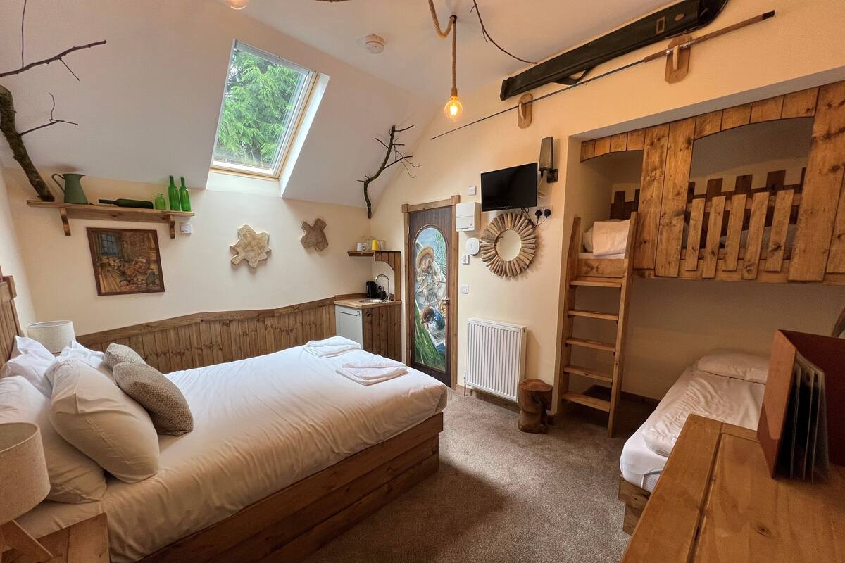 A cozy room with a wooden bed, a small kitchenette, a window, and a wooden ladder.