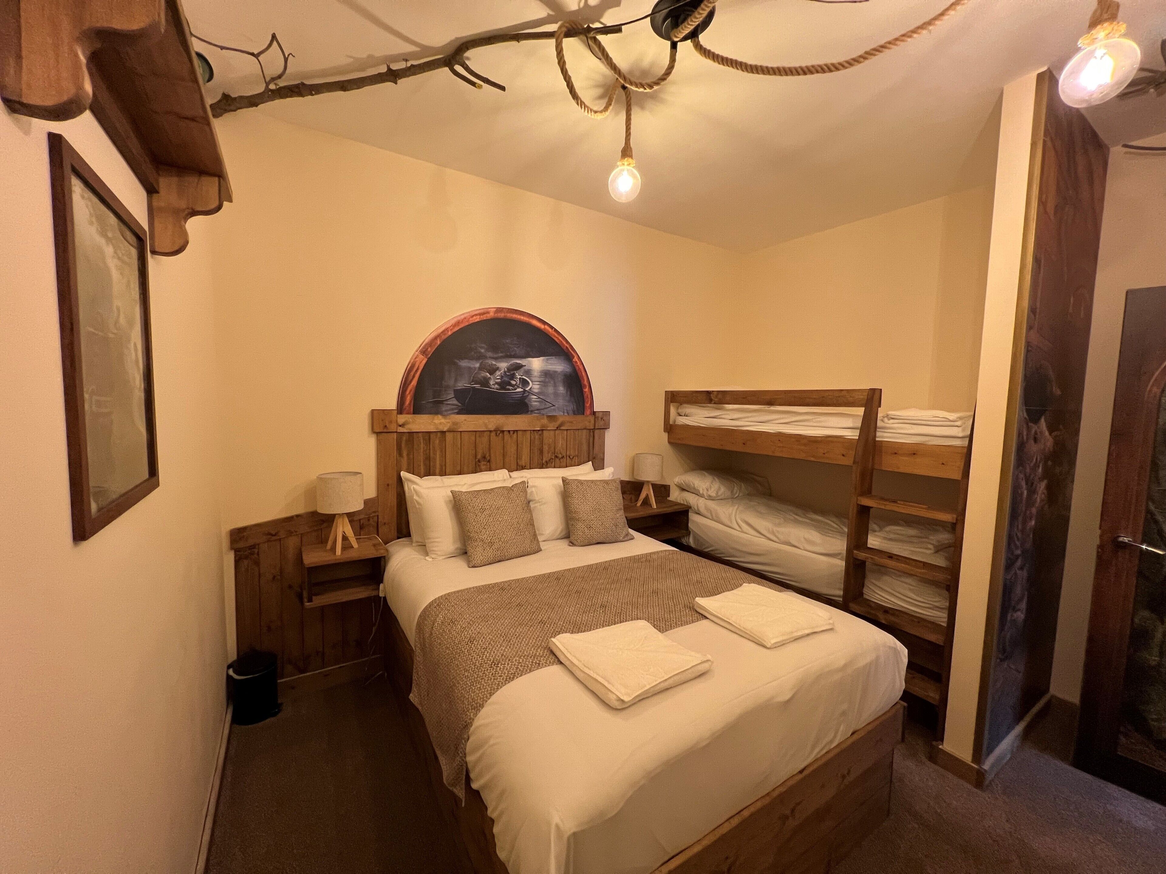 Ein Schlafzimmer mit Etagenbett, einem Einzelbett, einem Holzkopfende, einem Nachttisch, einer Lampe und einem gerahmten Bild an der Wand.