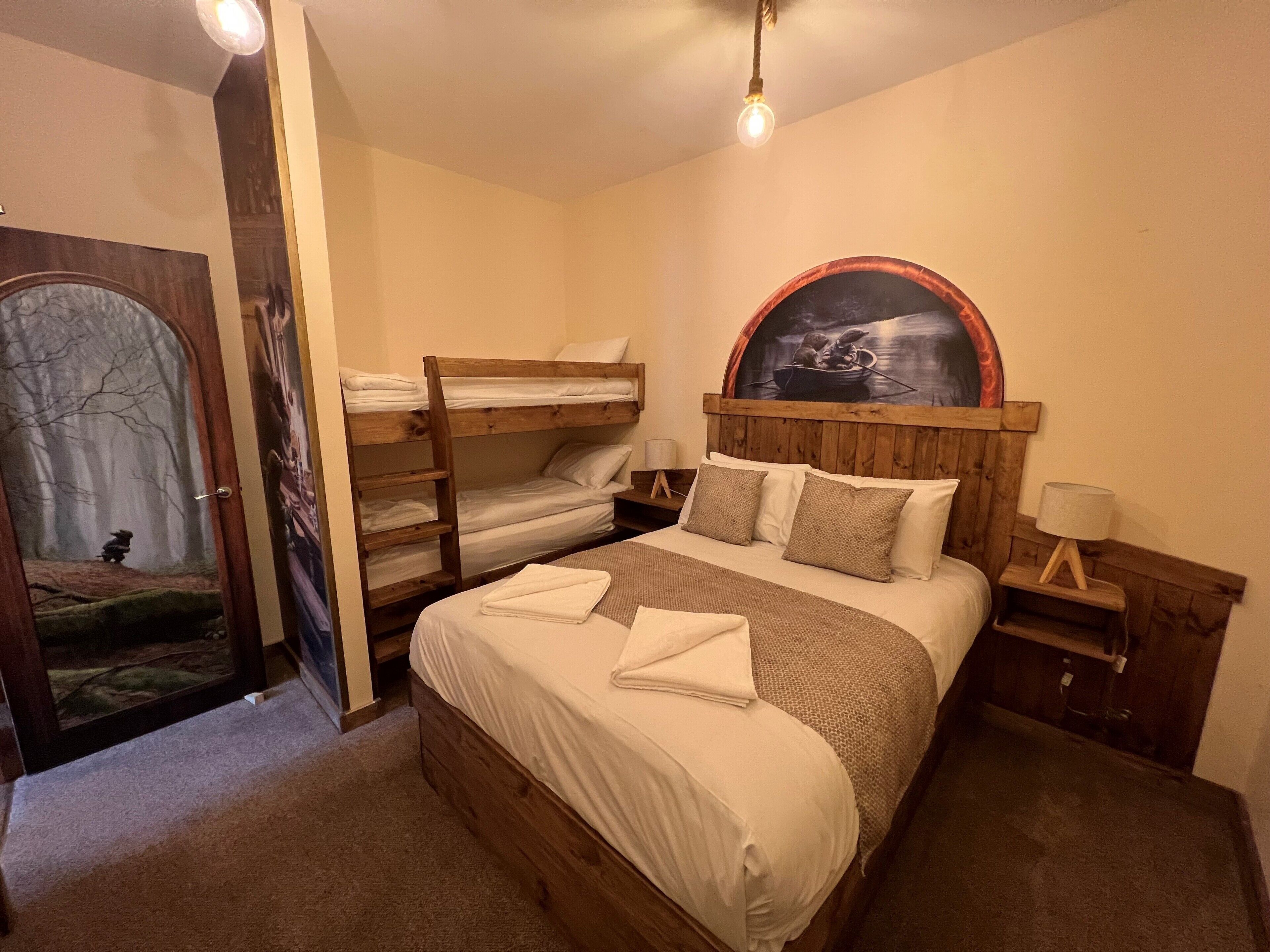 Habitación con literas, cabecera de madera, un cuadro sobre la cama, mesita de noche y una puerta con espejo.