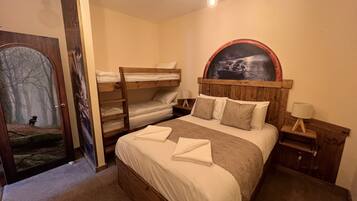 Habitación con literas, cabecera de madera, un cuadro sobre la cama, mesita de noche y una puerta con espejo.