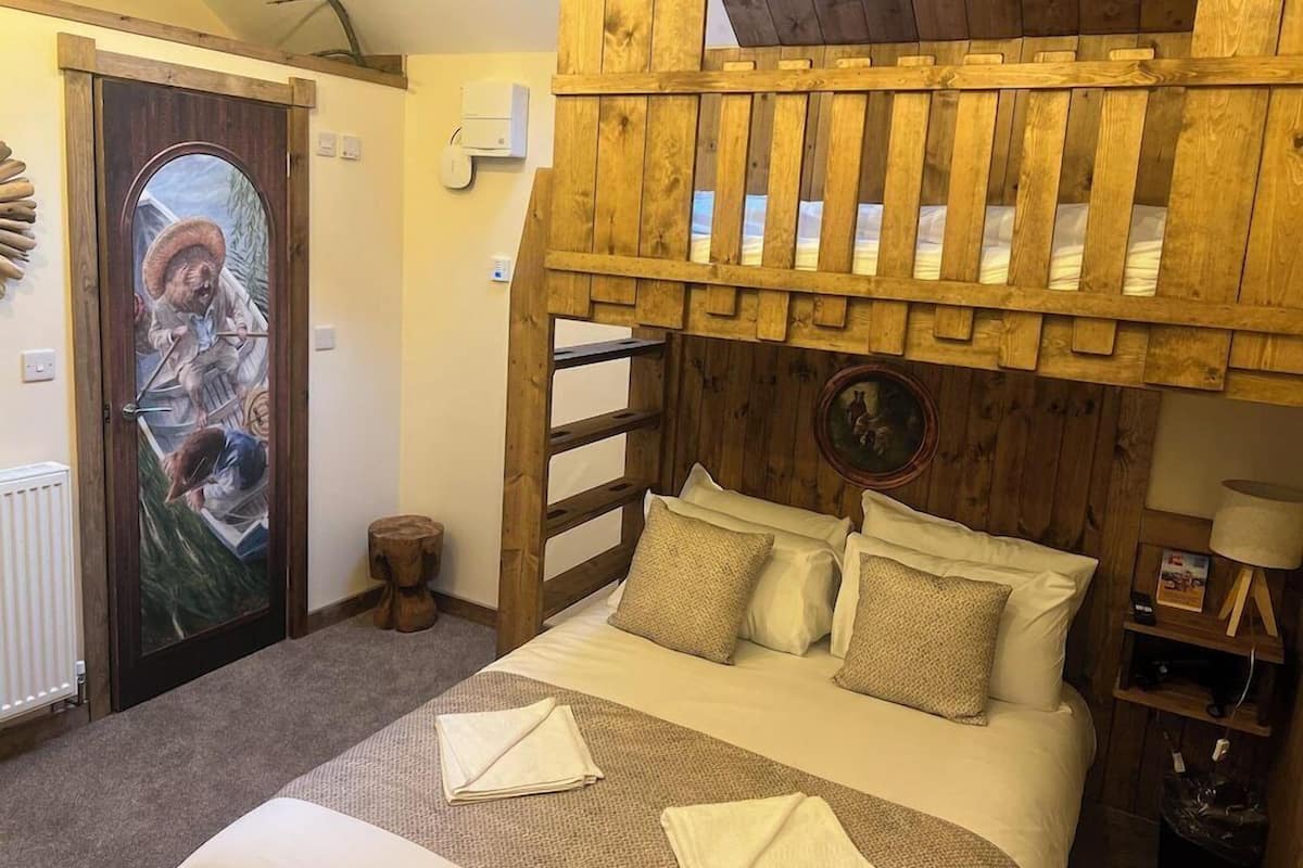 A rustic room with a bed, wooden headboard, a door with a painting, and a small stool.
