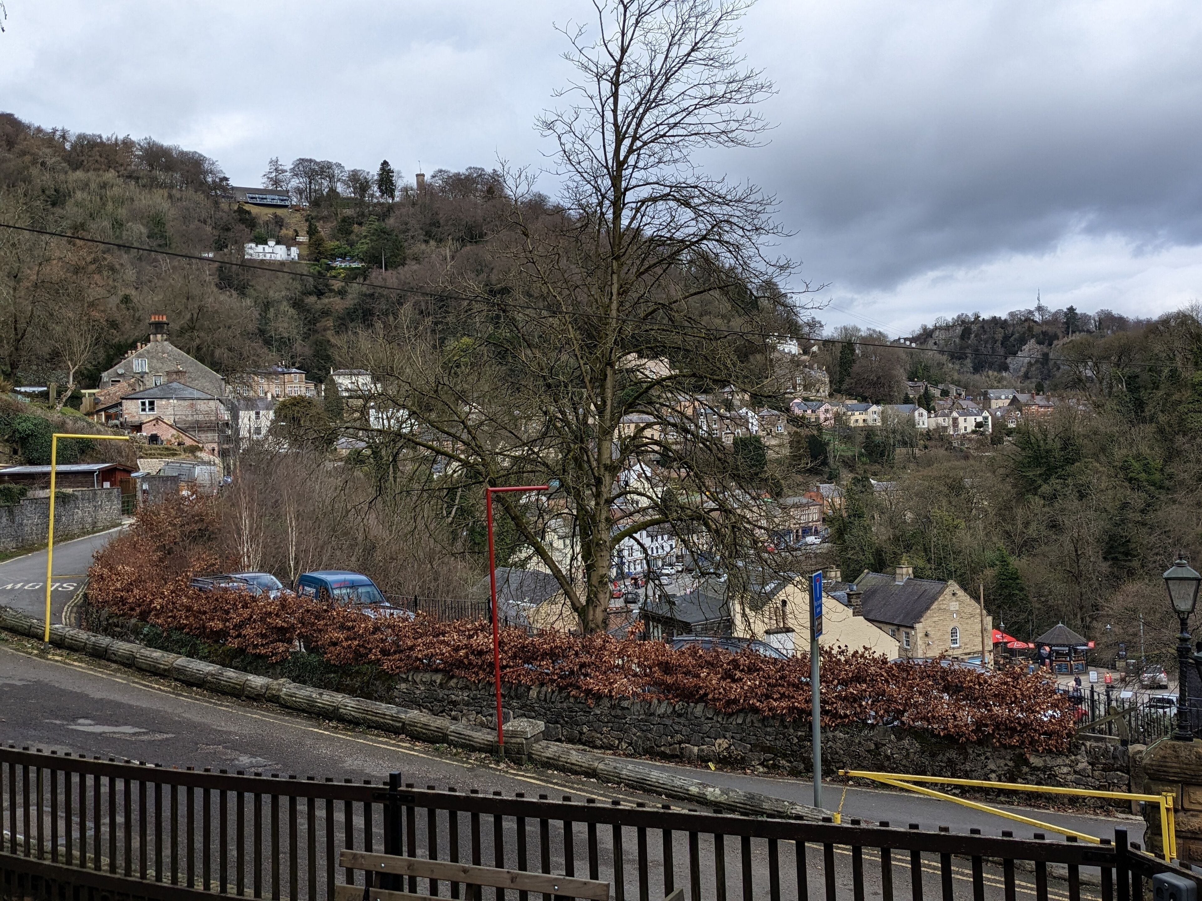 Vista de un pueblo con casas, un árbol destacado y un muro de piedra.