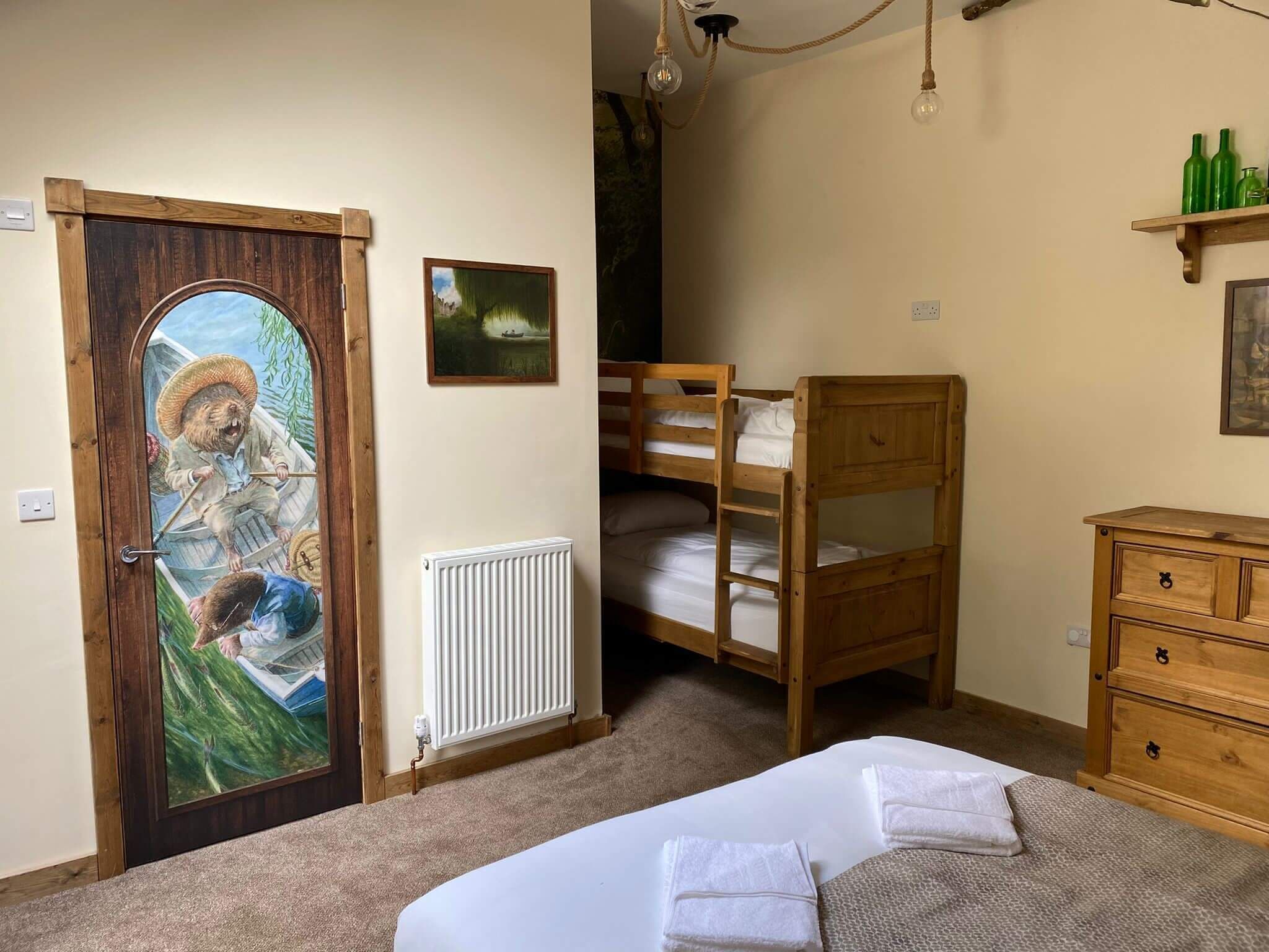 A cozy room with a bunk bed, a wooden dresser, a radiator, and a door with a mural.