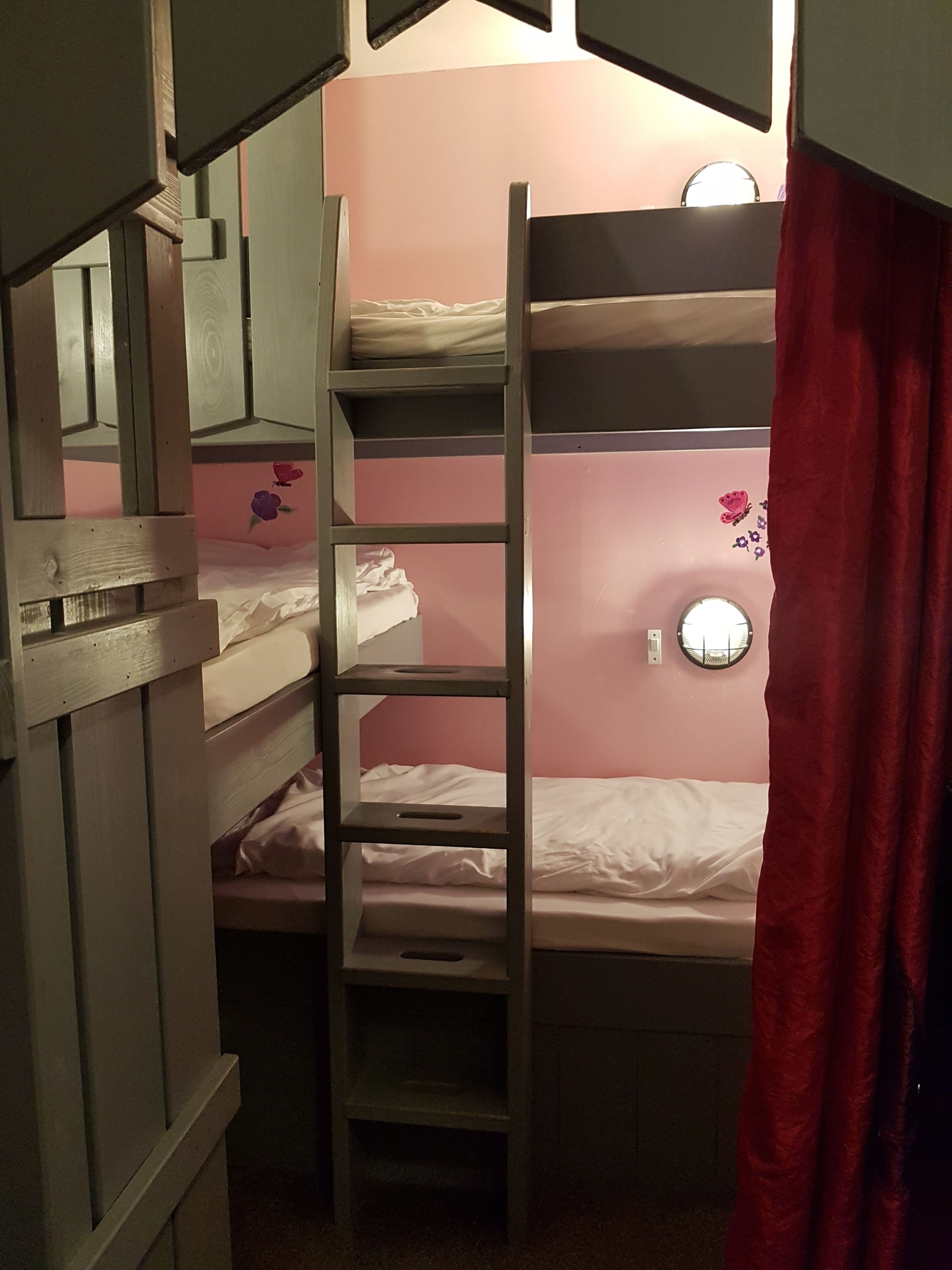 A bunk bed room with a ladder, a round wall clock, and a window with a curtain.