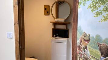 A bathroom with a wooden frame, a white toilet, a sink with a mirror, and a wall-mounted light switch.
