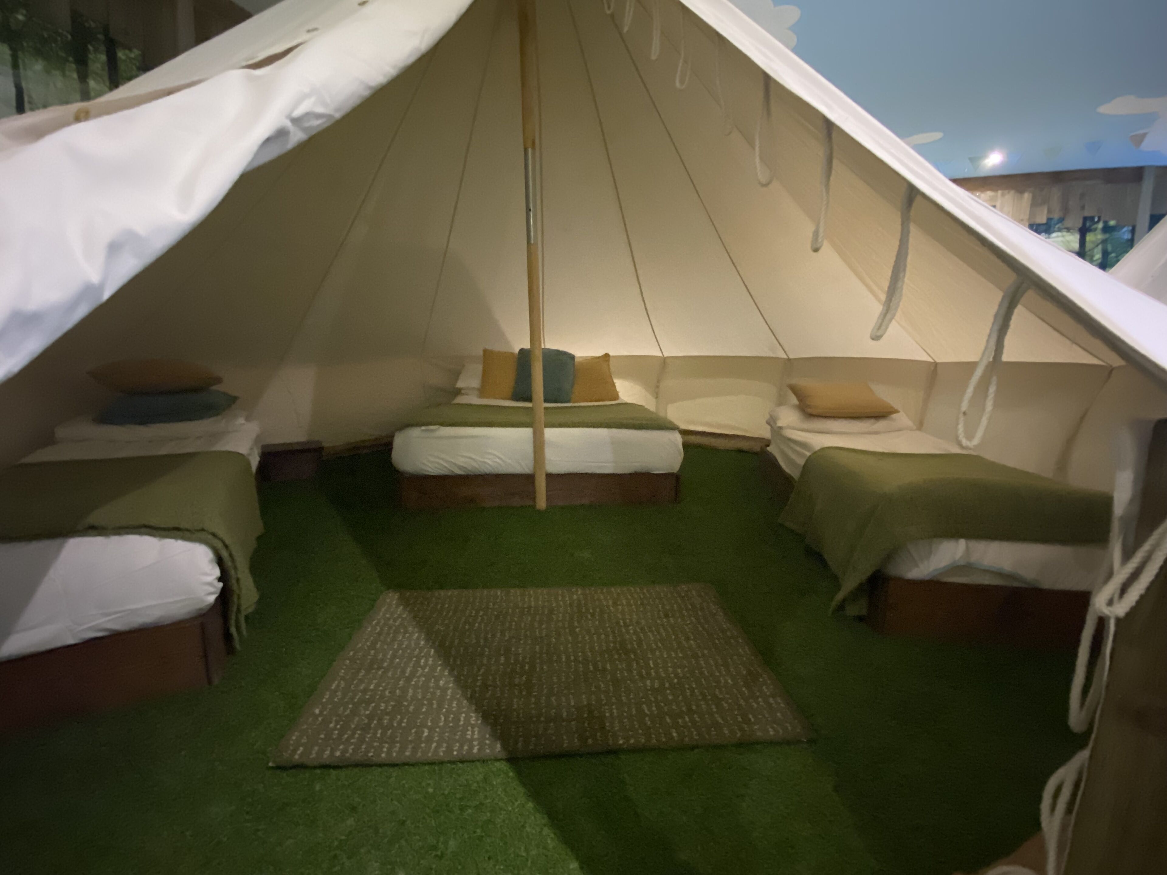 A tent-style room with two beds, a central bed, and a small table.