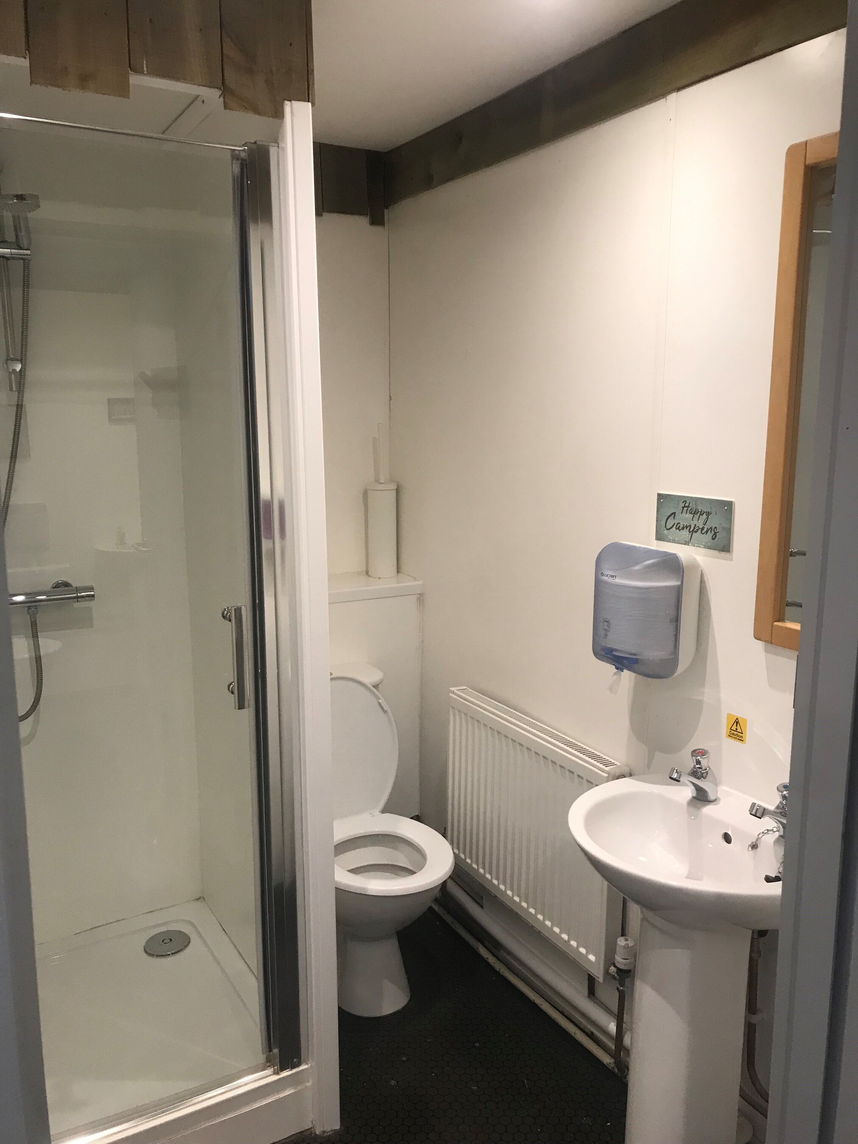 A bathroom with a glass shower enclosure, a toilet, and a sink with a hand dryer.