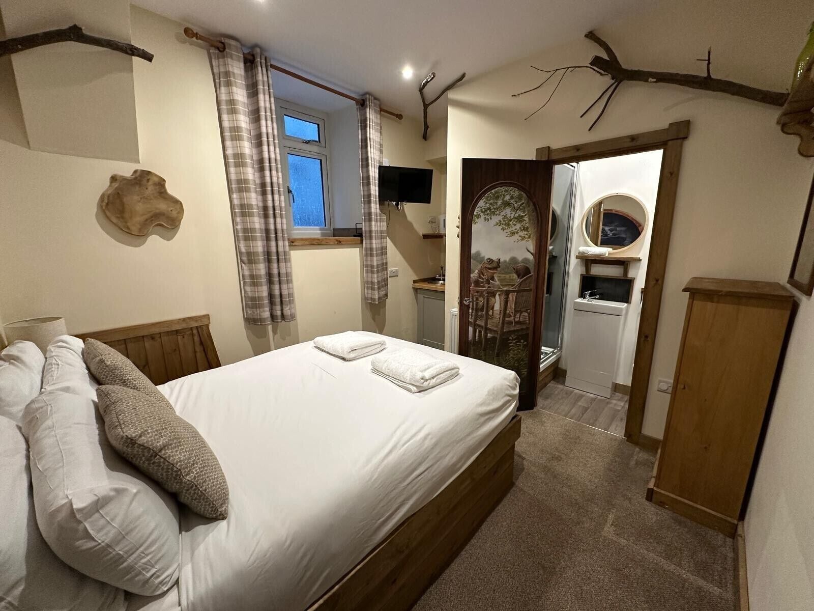 A bedroom with a bed, a mirror, a window with curtains, a wooden headboard, and a wall-mounted clock.