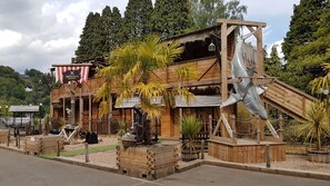 A wooden building with a pirate-themed sign, a large shark sculpture, and tropical plants.
