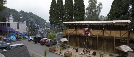 A rustic wooden building with a flag, a playground with slides, and a roller coaster in the background.