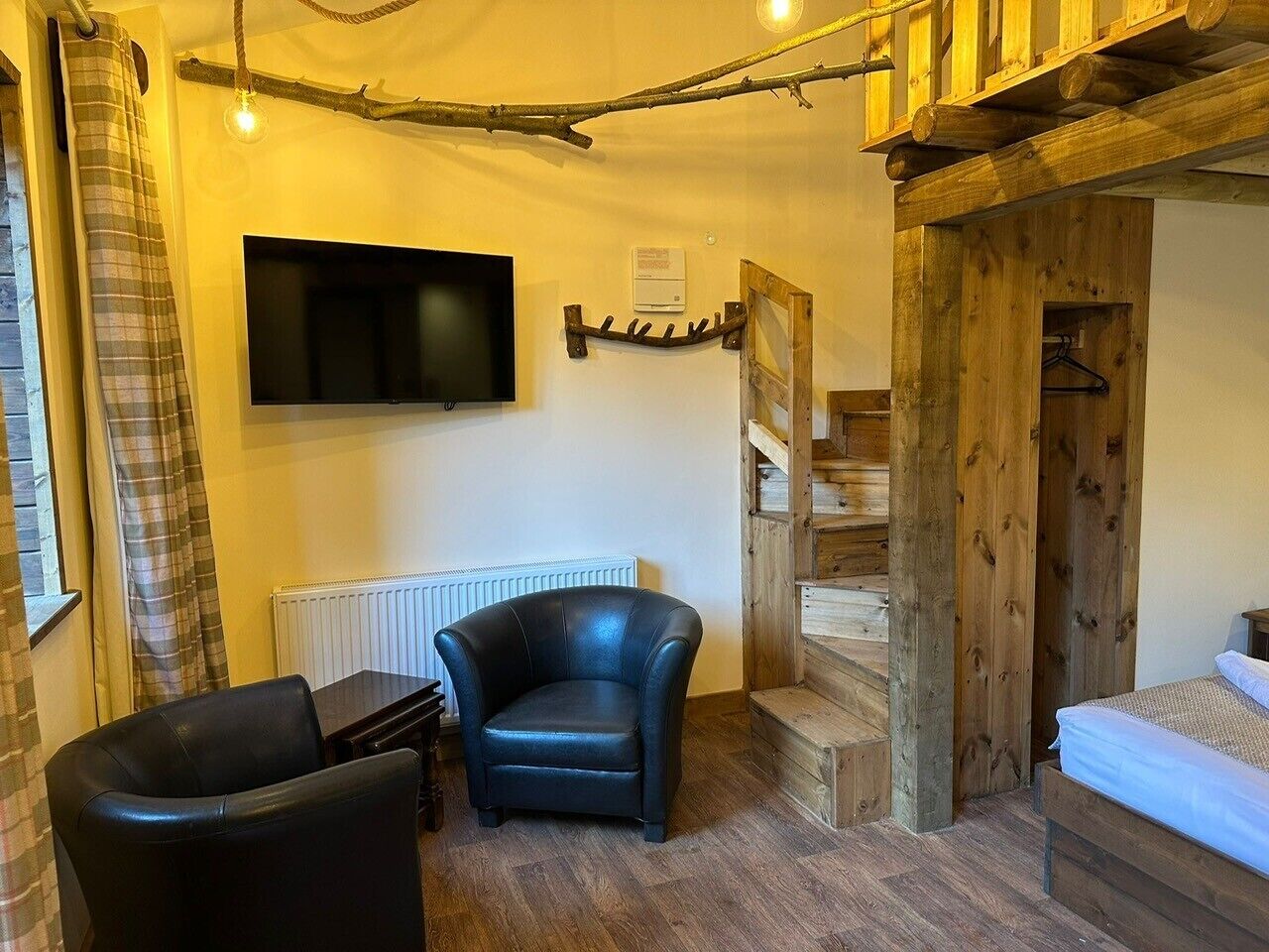 A cozy room with a bed, a chair, a TV, and a wooden staircase.