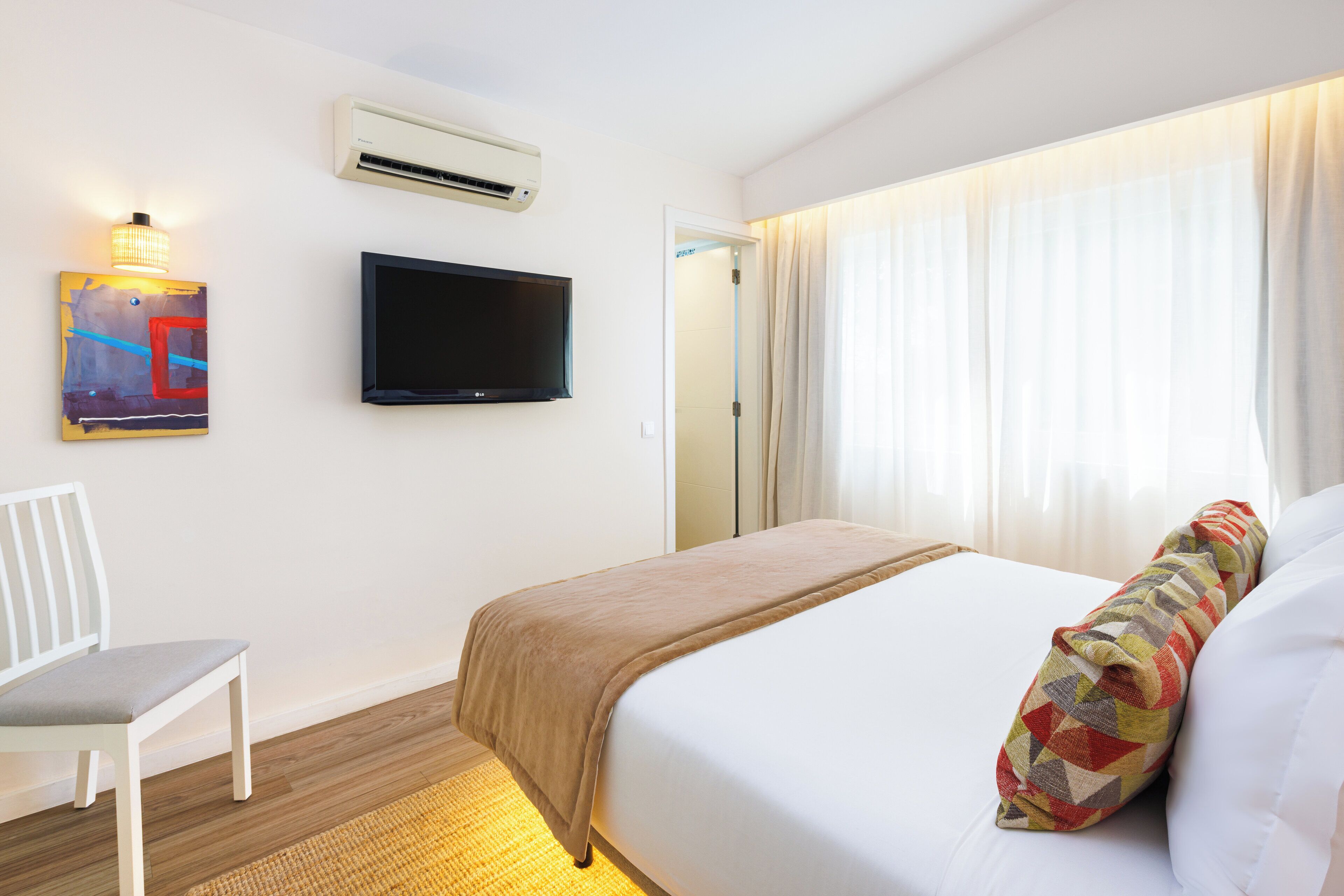 A hotel room with a bed, a television, a chair, and a painting on the wall.