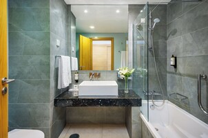 Un baño moderno con ducha de vidrio, lavamanos blanco y puerta de madera.