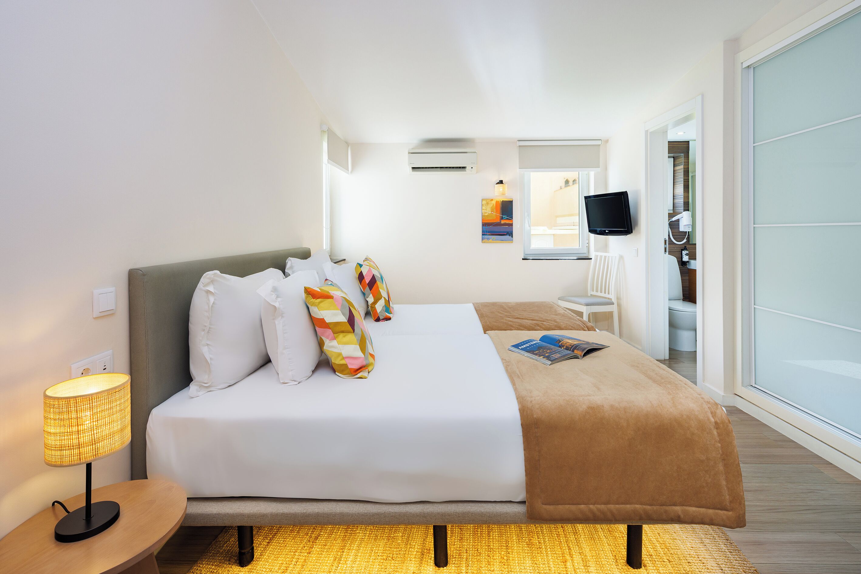 Habitación de hotel con cama, lámpara de noche, televisor de pantalla plana y ventana con vistas.