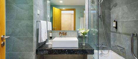 A modern bathroom with a glass-enclosed shower, a white sink, and a wooden door.