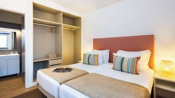 Una habitación de hotel con dos camas, un armario, un baño y una mesita de noche con lámpara.