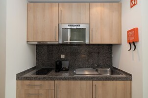 Cocina compacta con armarios de madera, horno de acero inoxidable, encimera de granito, cafetera y lavabo.