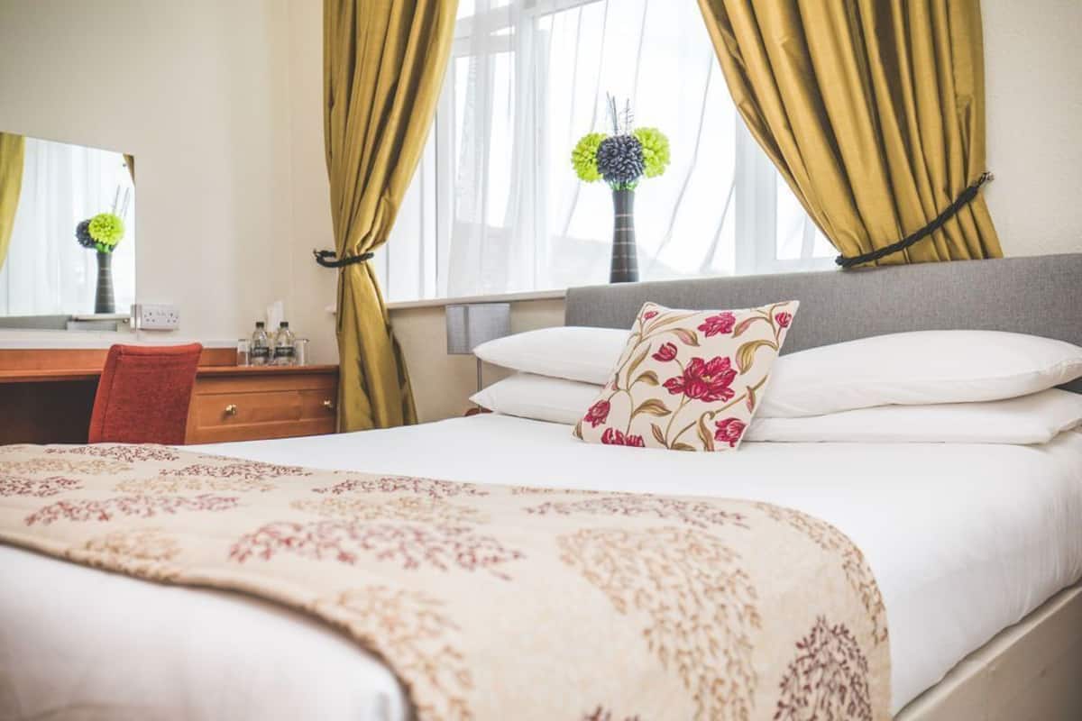 A hotel room with a bed, a desk, a chair, a vase with flowers, and curtains.