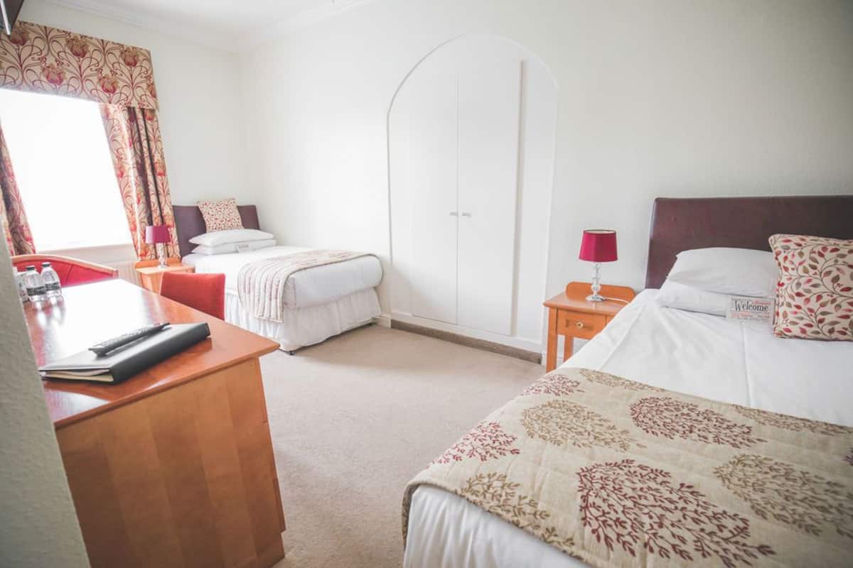 A hotel room with a desk, two beds, a wardrobe, and a window with curtains.