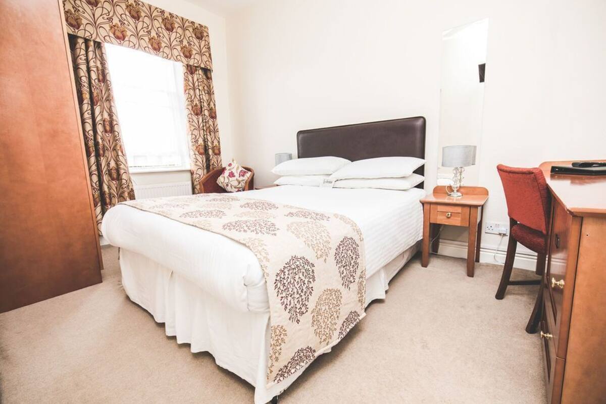 A bedroom with a bed, bedside table, lamp, chair, and a window with curtains.