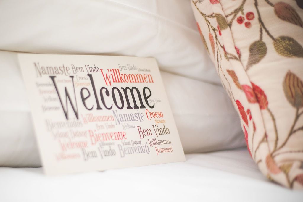 Tarjeta de bienvenida con saludos en varios idiomas sobre una cama.