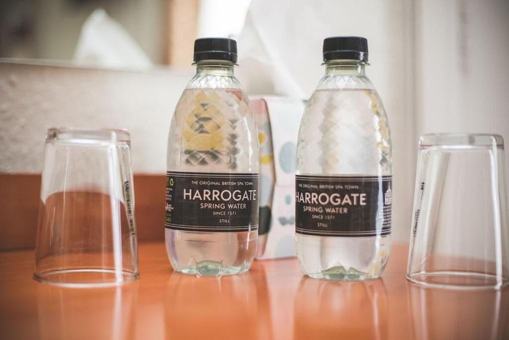 Tres botellas de agua Harrogate y dos vasos vacíos sobre una superficie de madera.