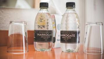 Tres botellas de agua Harrogate y dos vasos vacíos sobre una superficie de madera.