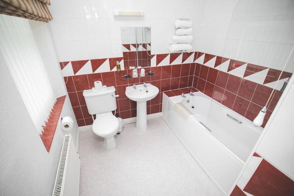 Un baño con inodoro, lavabo y bañera, con azulejos rojos y blancos.