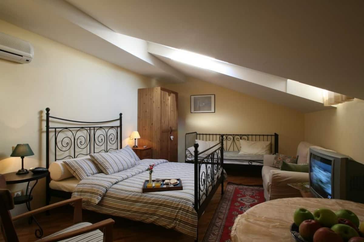 A cozy attic bedroom with two beds, a television, and a dining table with fruit.