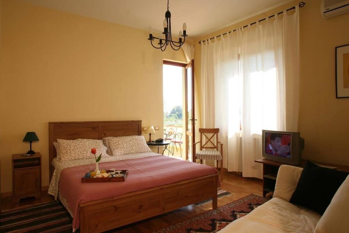 A bedroom with a wooden bed, a TV, a chair, and a small table.