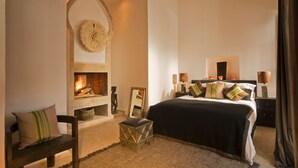 A bedroom with a fireplace, a bed with multiple pillows, a bench, and a small stool. - Maison Manzano  (Marrakech)