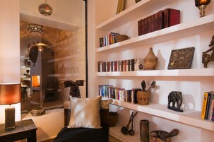 Un rincón acogedor para leer, con un sillón cómodo, una estantería llena de libros y adornos, y una lámpara sobre una mesita.