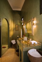 Un baño con un espejo grande, un lavamanos con grifo dorado y un jarrón con flores.