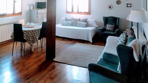 Een ruime woonkamer met hoog houten plafond, een eettafel met stoelen, een bank, een fauteuil en een lamp.