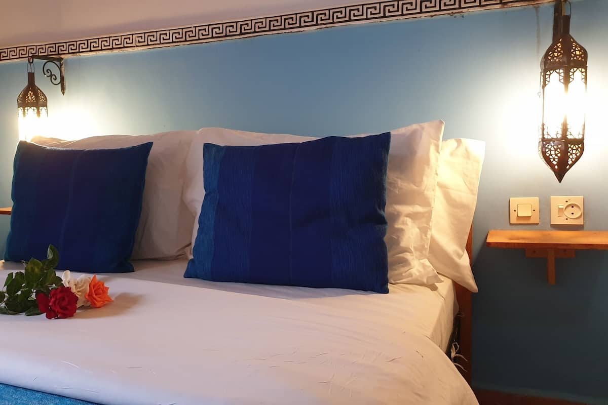 Ein Bett mit blau-weißen Kissen, ein Nachttisch mit Lampe und eine Wand mit dekorativer Bordüre.